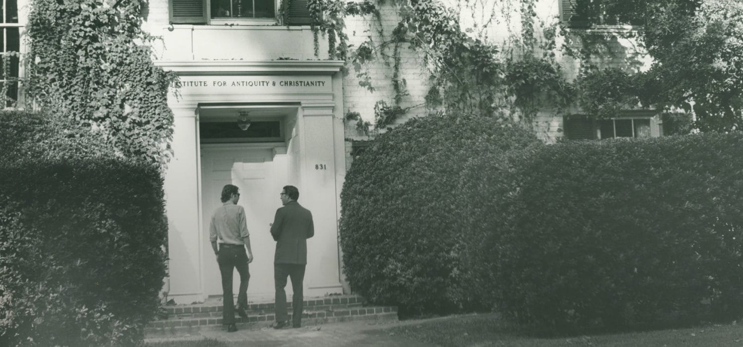 an old black-and-white photograph of two people walking into the Institute for Antiquity and Christianity building, now the house of School of Arts & Humanities
