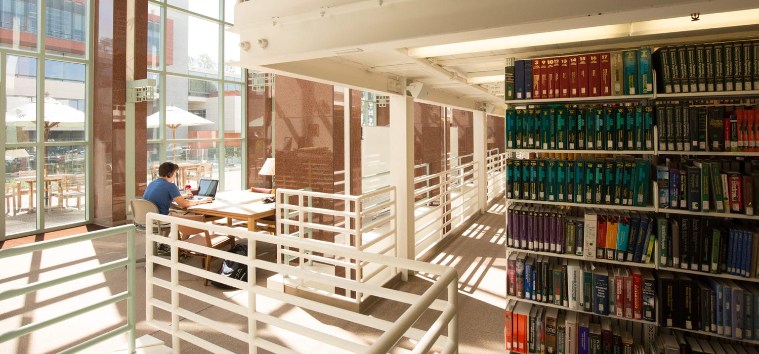 Student studies at a table next to the library stacks