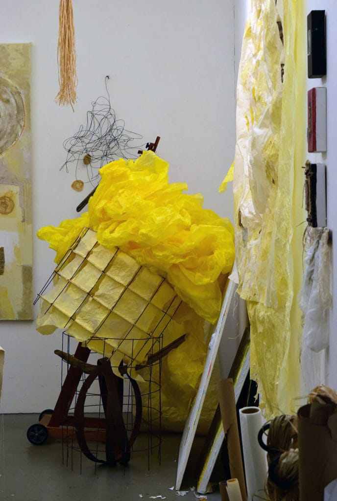 Student artwork by Adrienne DeVine, a room of yellow paper coming out of a black wire basket