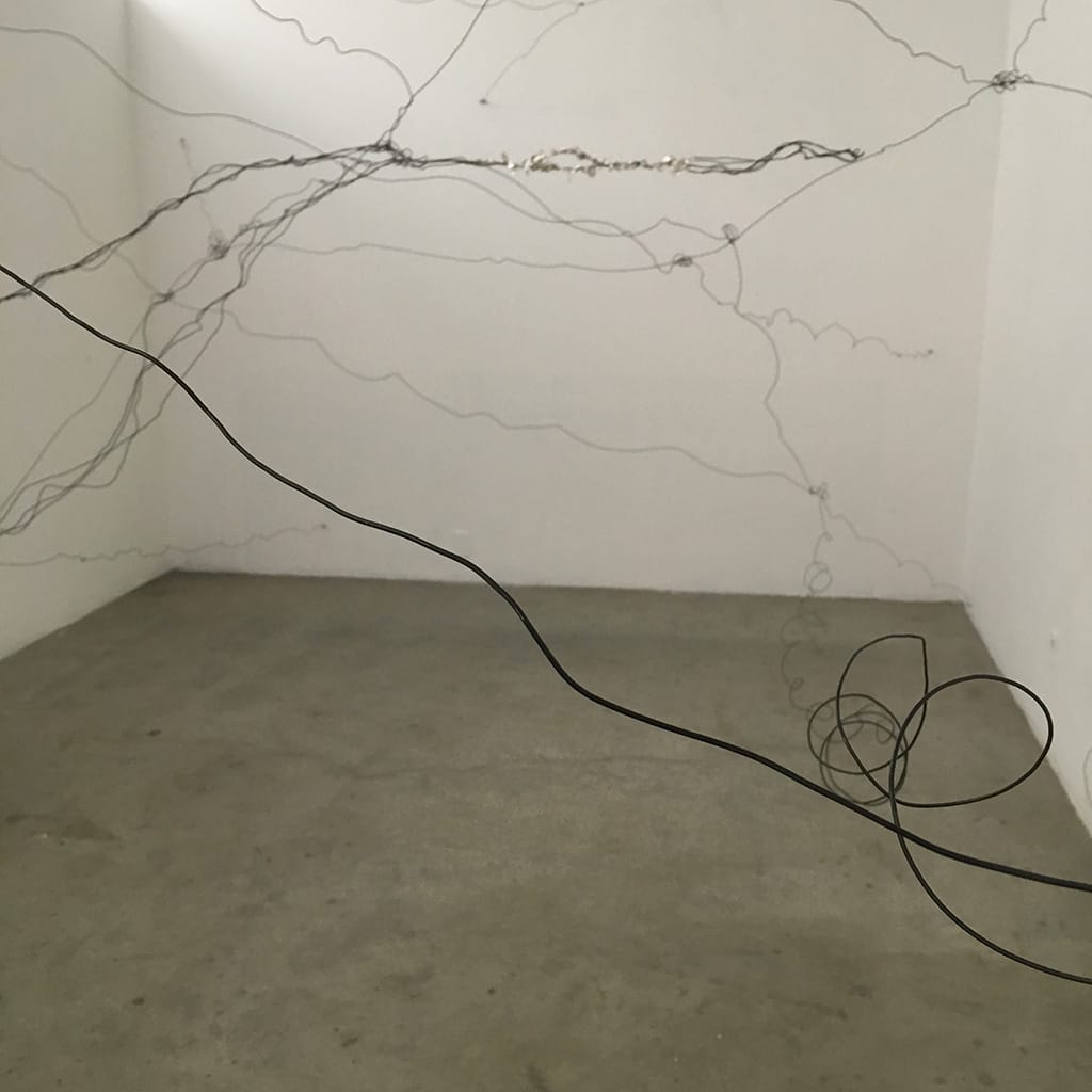 student artwork by Maya Luque entitled Shel:13.8. Black wire entangled throughout white walled room