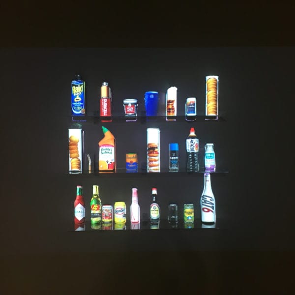 Student artwork by Chaoyi Stormy Wu, black wall with three shelves of household products brightly lit