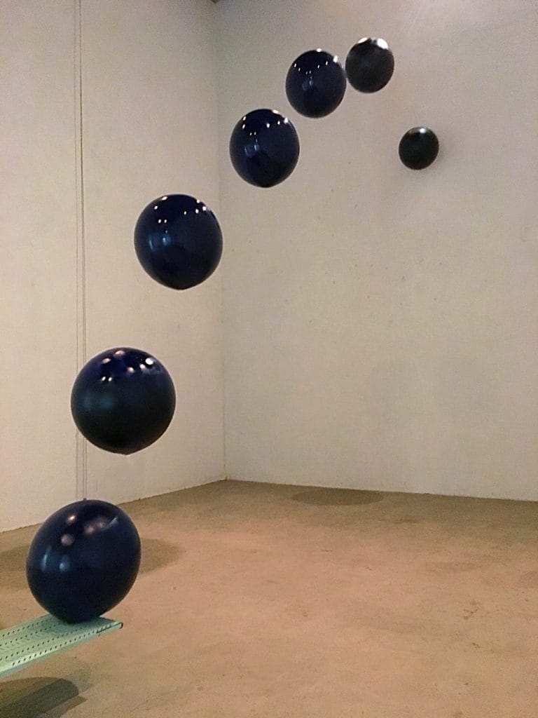 Student artwork by Rafaella Suarez, balls curving up to a wall from a board on the ground
