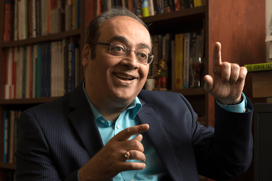 Samir Chatterjee in front of book shelf with a large smile
